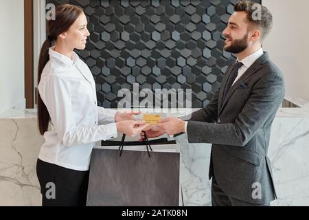 Handsome young bearded businessman in jacket making cashless payment while buying clothes in store Stock Photo