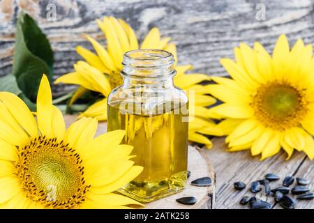 Sunflower oil in a glass jar with seeds and fresh flowers on a wooden background. Healthy foods and fats. Organic and eco food. Stock Photo