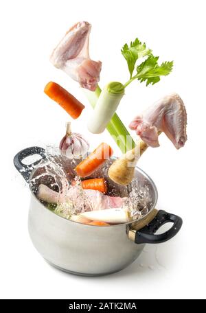 Ingredients for making broth flying towards a pot with splashing water on white background Stock Photo
