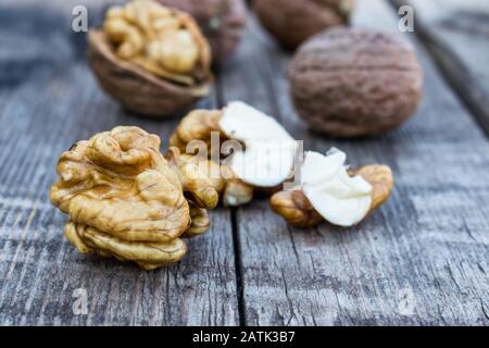 Peeled walnuts and walnut kernels lie on a rustic old wooden table. Harvest walnuts. Stock Photo