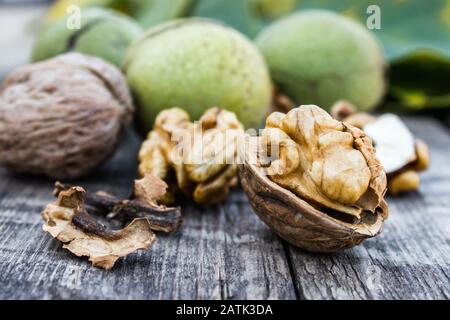Walnut kernels and whole walnuts lie next to nuts in green shells and green leaves on a rustic old wooden table. Harvest walnuts. Stock Photo