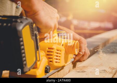 Male hands worker hold electric work planer with wooden board, smooth dust Stock Photo