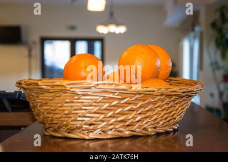 A wicker basket full of oranges, fresh citrus fruits on wooden table in a kitchen Stock Photo