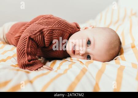 Beautiful little baby girl on the bed in a cozy sweater smiles. Concept of motherhood and childhood. Adorable six month old baby girl lying on the bad and looking into the camera Stock Photo - Alamy
