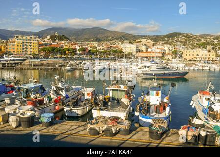 Scenic view of the harbor with fishing boats and luxury yachts docked at the piers and the coastal town in the background, Sanremo, Liguria, Italy Stock Photo