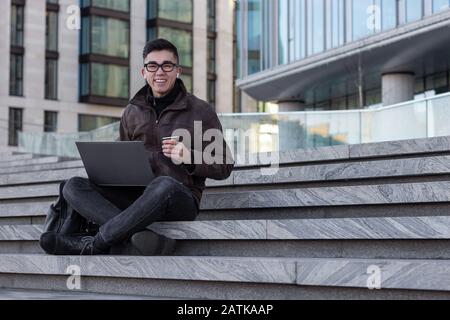 happy male Asian student programmer freelancer smile with laptop and drink Stock Photo