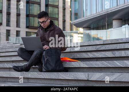 young successful Asian student programmer sit on the steps of the office laptop Stock Photo