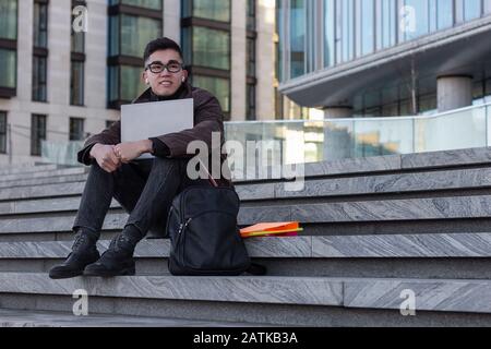 young successful Asian student programmer sit on the steps of the office laptop Stock Photo