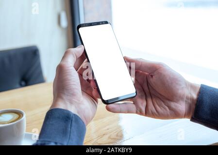 Mockup image of hands holding modern black mobile phone in coffee shop Stock Photo