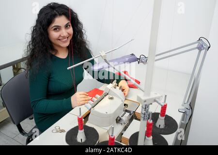 Young woman using professional overlock sewing machine in workshop. Equipment for edging, hemming or seaming clothes at tailors shop Stock Photo