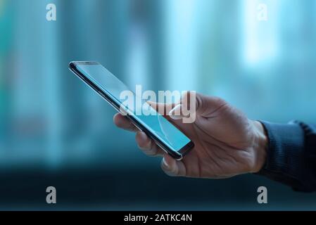 Phone in man hand. Blue windows, business center in background. Concept of mobile technologies global use Stock Photo
