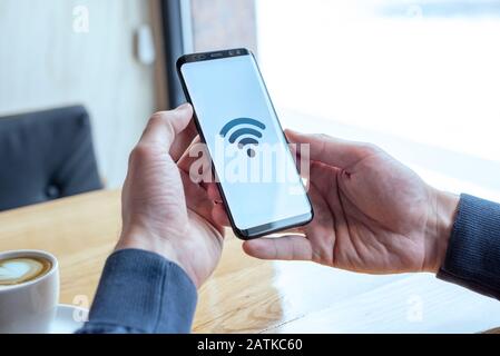 Wi-fi concept icon on smart phone display. Hands holding mobile phone in coffee shop. The concept of free internet and global connection Stock Photo