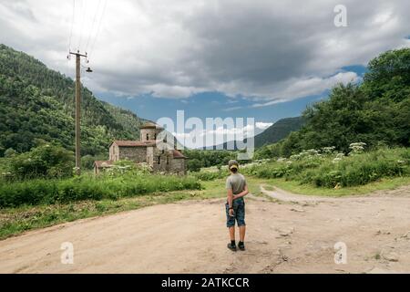 A boy standing at a crossroads in the mountains in front of an old church Stock Photo