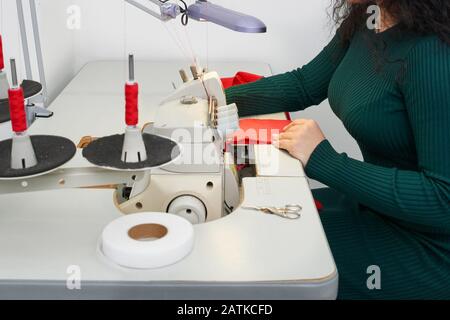 Young woman using professional overlock sewing machine in workshop. Equipment for edging, hemming or seaming clothes at tailors shop Stock Photo