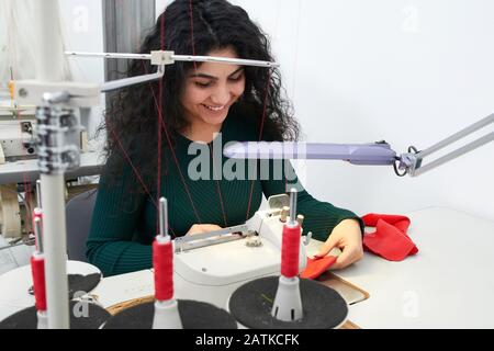 Young woman using professional overlock sewing machine in workshop. Equipment for edging, hemming or seaming clothes at tailors shop Stock Photo