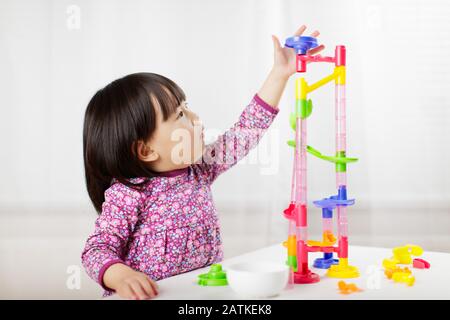 toddler girl play marble run game at gome agianst white background Stock Photo