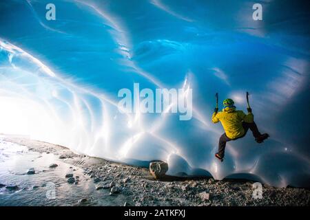 Man ice climbing on glacial ice in ice cave. Stock Photo