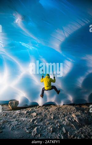 Rear view of man ice climbing in glacier cave. Stock Photo