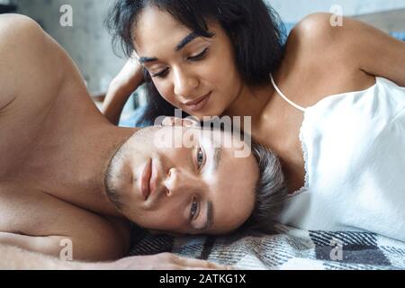 Mixed Race Couple. Young woman looking at man tender at home lying on bed close-up Stock Photo