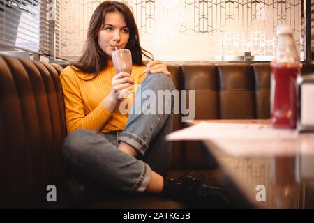 Thoughtful teenage girl drinking chocolate milkshake in restaurant Stock Photo