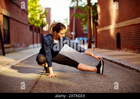 A female runner stretches on a city street. Stock Photo