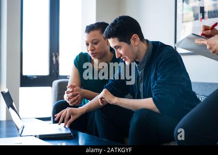 Female colleague looking at businessman using laptop on table in office Stock Photo