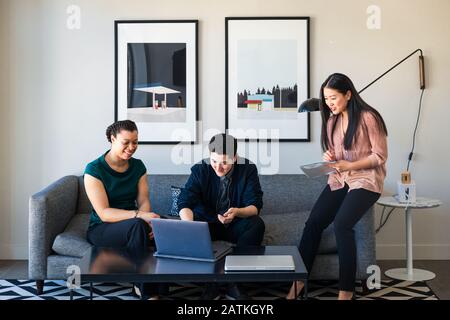 Male and female colleagues discussing over laptop while sitting on sofa at office Stock Photo