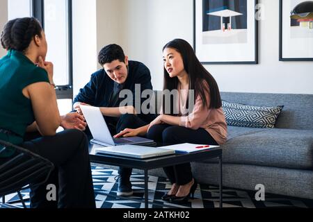 businesswoman discussing over laptop while coworkers at table in office Stock Photo