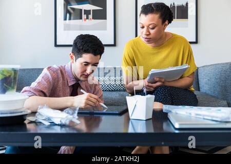 businesswoman looking at male colleague using graphics tablet while sitting at table in office Stock Photo