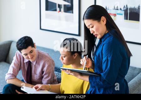 businesswoman using graphics tablet while coworkers discussing over documents in office Stock Photo
