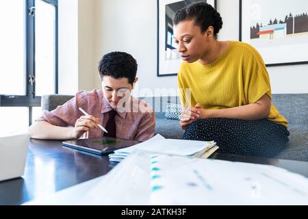 Female colleague looking at businessman using graphics tablet while sitting in office Stock Photo