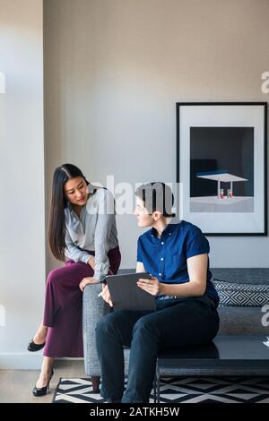 Male and female business coworkers planning over graphics tablet on sofa against wall at office Stock Photo
