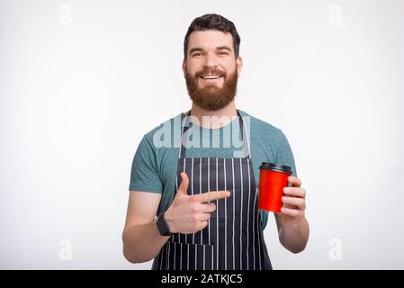 Happy bearded Barista standing over white background and pointing at cup of coffee to go Stock Photo
