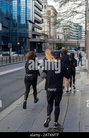 Mixed group of Sunday morning runners or joggers in black matching outfits practising running or jogging in Lower Thames Street, London, UK Stock Photo