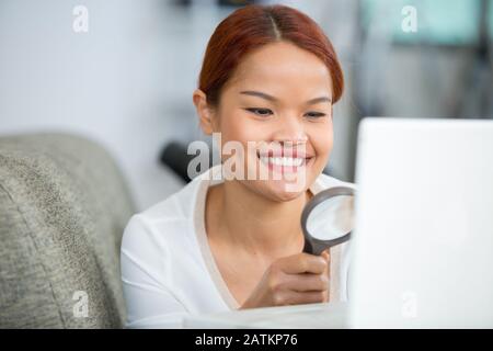 asian woman looking through magnifying glass and using laptop Stock Photo