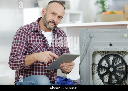 man using tablet pc to fix washing machine Stock Photo