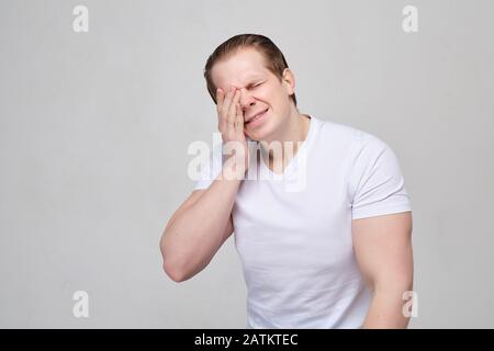 A man with a white T-shirt rubs his eyes in pain. Human vision problems. close up. Stock Photo