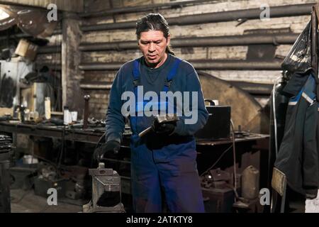 aged male blacksmith chooses a hammer to start working in a workshop getting ready for work Stock Photo