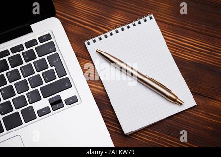 A notebook with a pen lies next to a laptop on a wooden table. Close up. Stock Photo