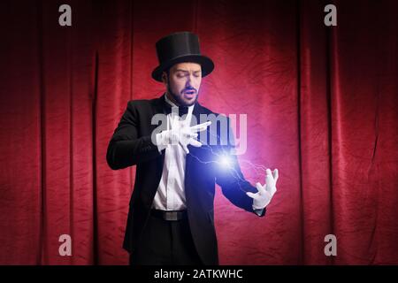 Magician performing a trick and producing electricity on a stage with red curtain Stock Photo