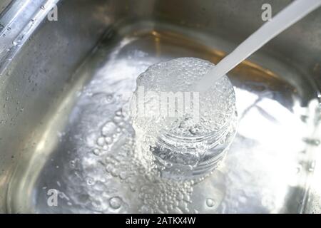 Water from tap into plastic container and it overflow to the sink. Save water concept. Stock Photo