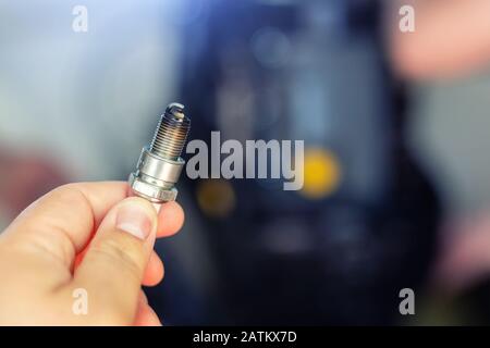 Machanic hand holding used dirty spark plug with disassembled boat engine on background during repair. Seasonal motor service and maintenance Stock Photo
