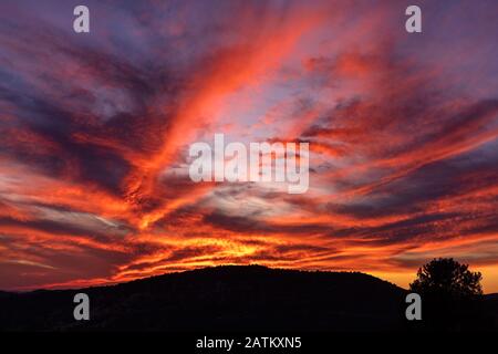 Colorful sunset sky with dramatic clouds and mountain silhouette in the background. Stock Photo