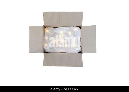 Opened cardboard box with crumpled wrapping paper and lights garland. Holiday online shopping concept. Top view. Isolated on white. Stock Photo