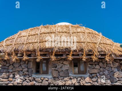 Folk Village in South Korea. Beautiful walls are made from stones. Thatch roof is in a good condition. Two small windows are looking like eyes. Stock Photo
