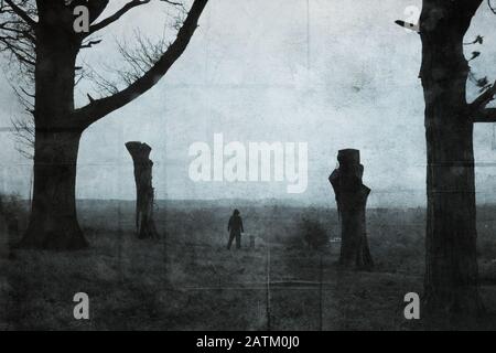 A scary dark hooded figure standing between two trees in the countryside. With a digital paint effect. With a grunge, textured edit. Stock Photo
