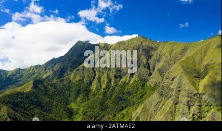 View from above, stunning aerial view of a green mountain range surrounded by clouds and a beautiful blue sky in the background. Sembalun, Lombok. Stock Photo