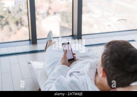 Relax in the hotel with a phone in hand. A man lying on a lounger by the pool and enjoying smartphone and great city view in front of him Stock Photo
