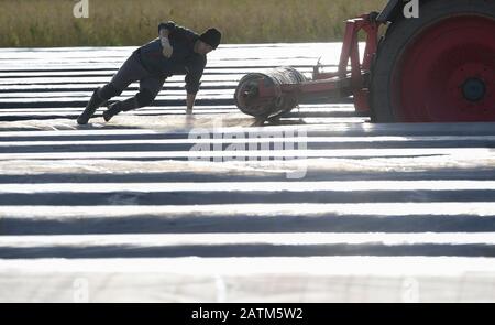 Weiterstadt, Germany. 03rd Feb, 2020. Workers at Weiterstädter Tannenhof  draw a transparent foil over an asparagus spider so that minnitunnels can  be placed on asparagus ridges with the help of metal poles.