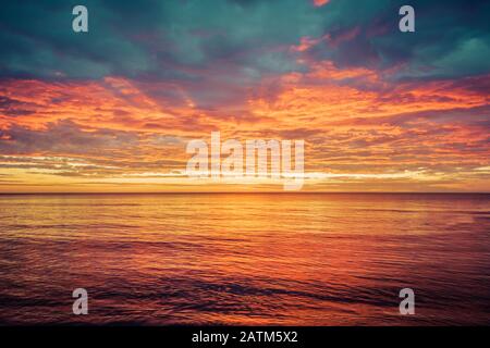 Picturesque sunrise over the sea. Dramatic sky colored in orange and red. Stock Photo